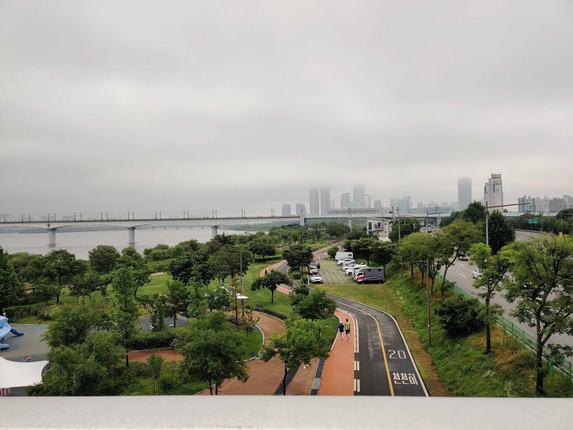 A runner on the curving Han River path on a green summer evening in Mapo.