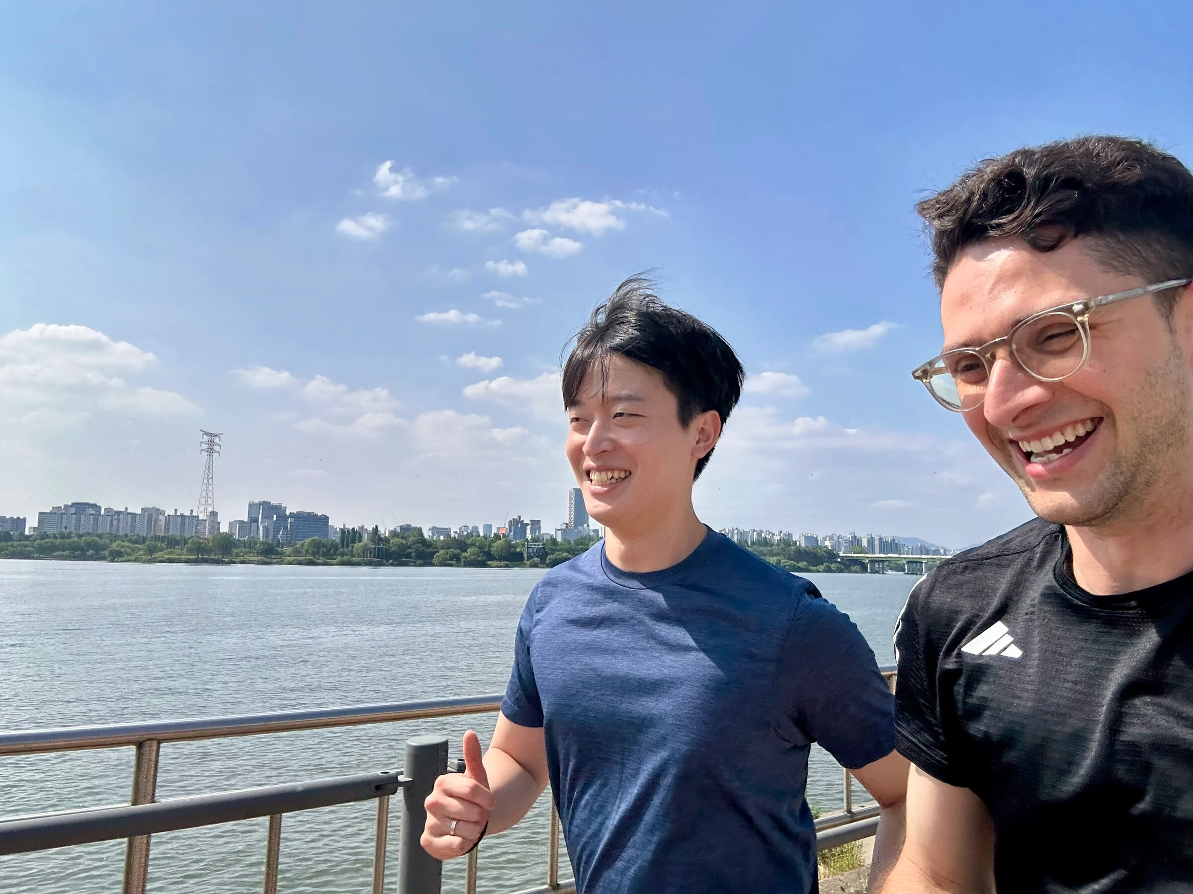Quintin and a running guest side by side on the Han River path, both smiling, with the Seoul skyline across the water.